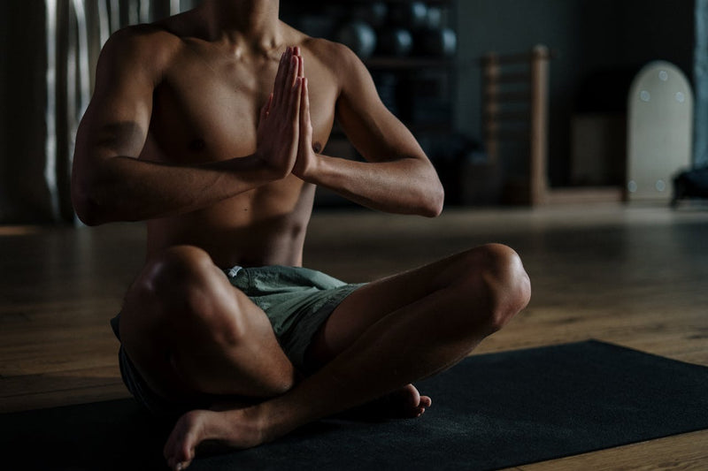 Fit man practicing yoga in a dimly lit room shirtless