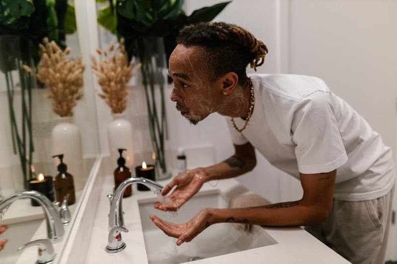 Man applying skincare in a bathroom with plants and candles in the background